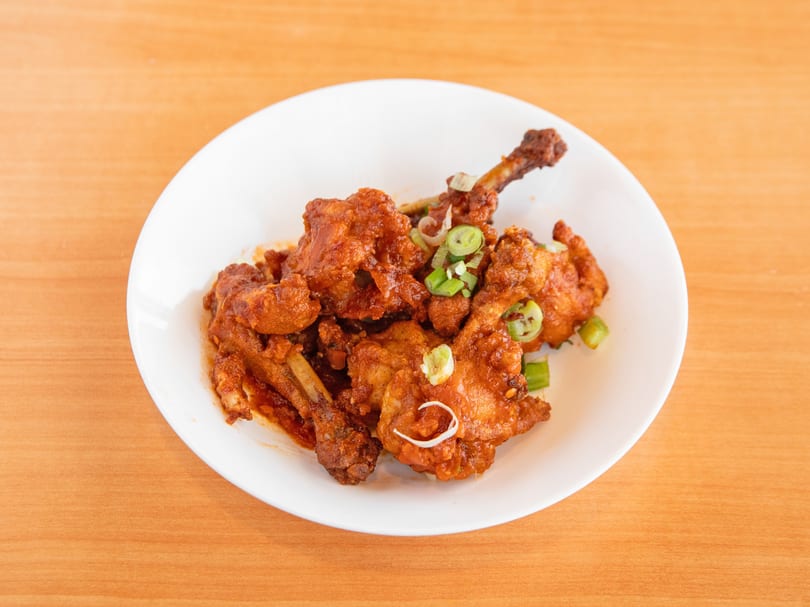 A white plate filled with crispy, saucy chicken lollipops garnished with sliced green onions.
