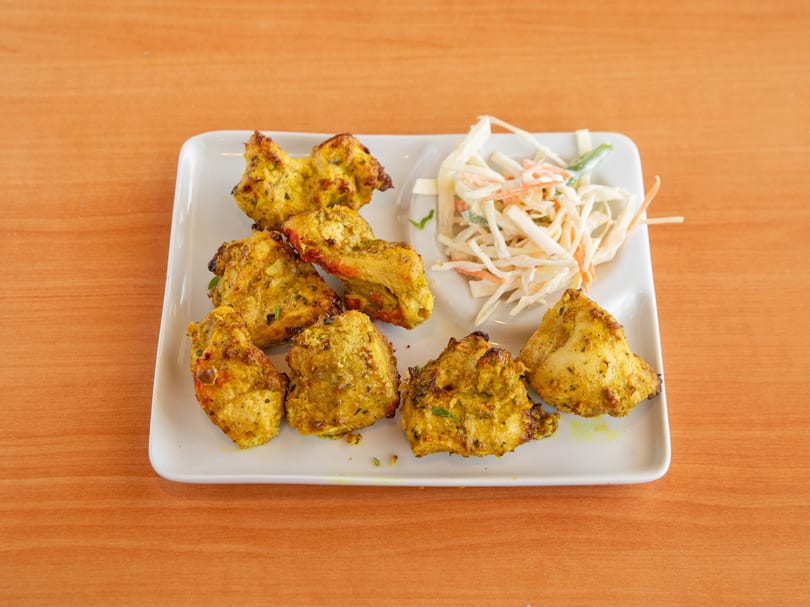 Golden-brown chicken tikka pieces and coleslaw on a white rectangular plate on a wooden table.